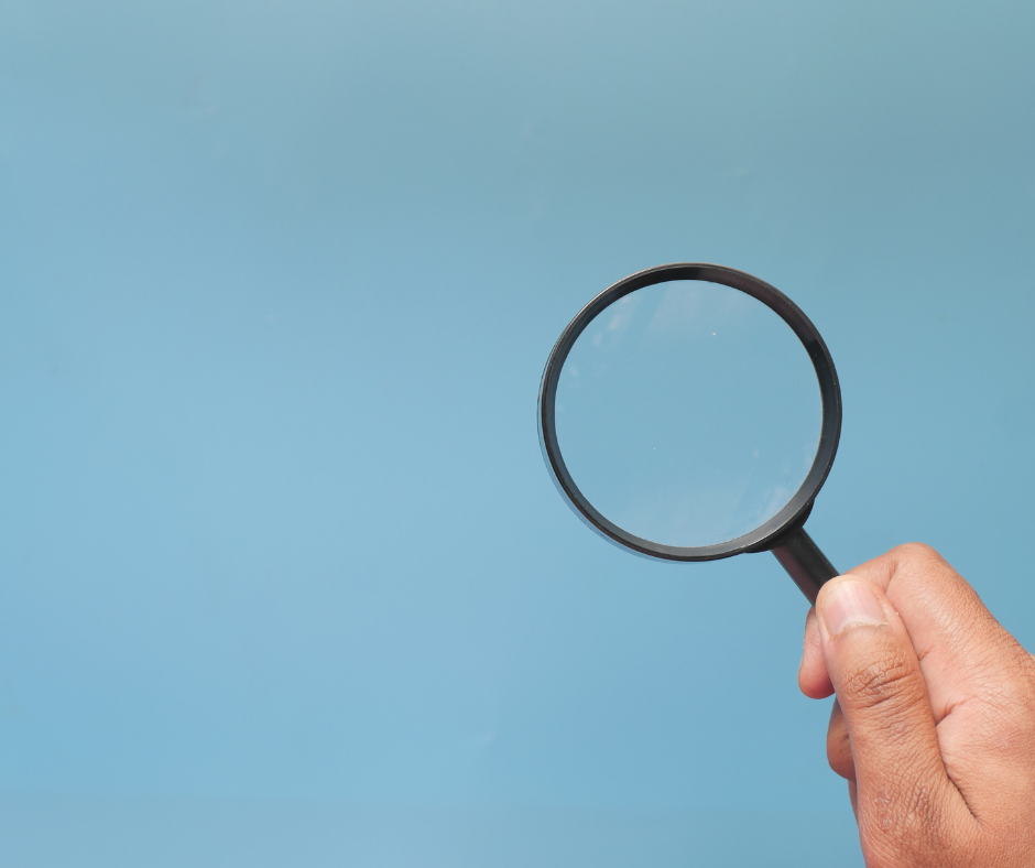 Hand holding magnifying glass against blue background