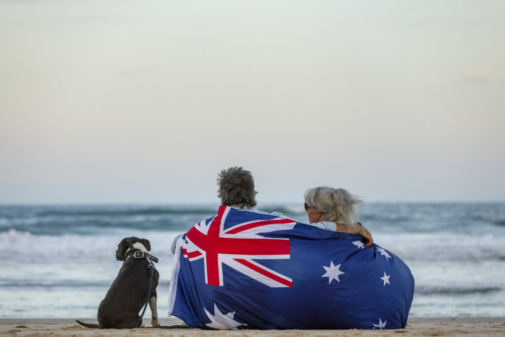 Couple wrapped in Australian flag on beach with dog
