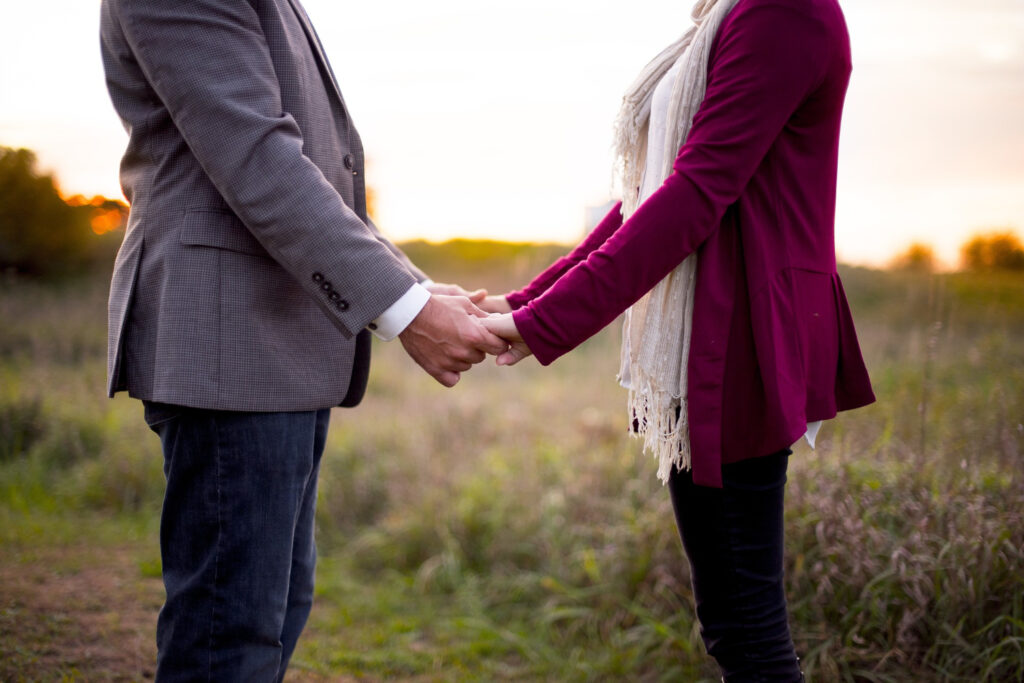 Couple holding hands in a field at sunset.