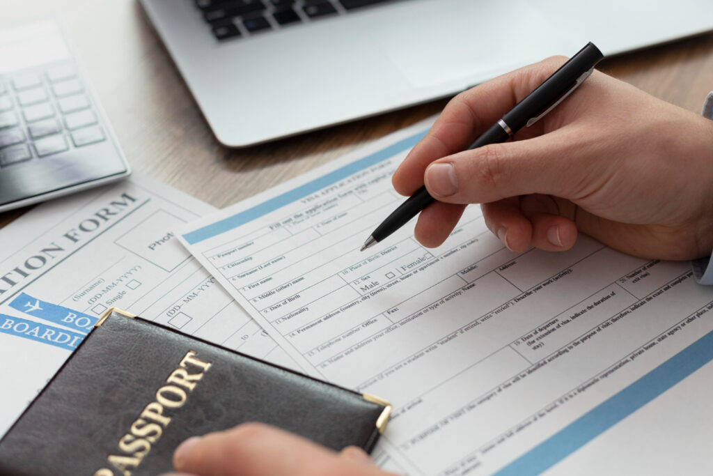 Person filling out a visa application form with a passport and pen.