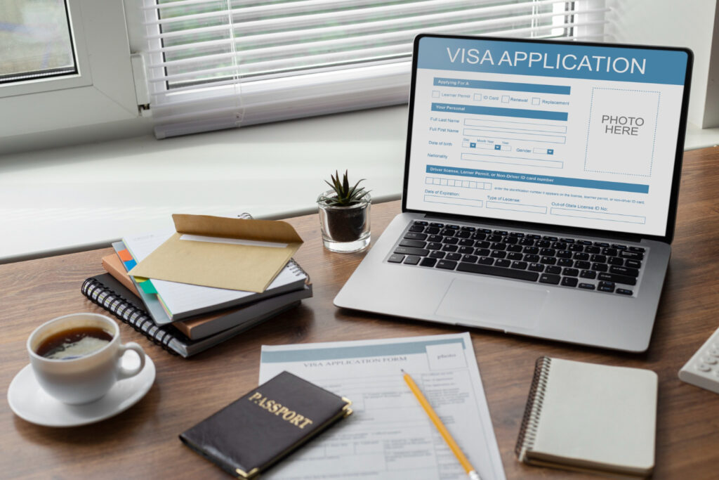Laptop displaying a visa application form, passport, and paperwork. Immigration lawyer services.
