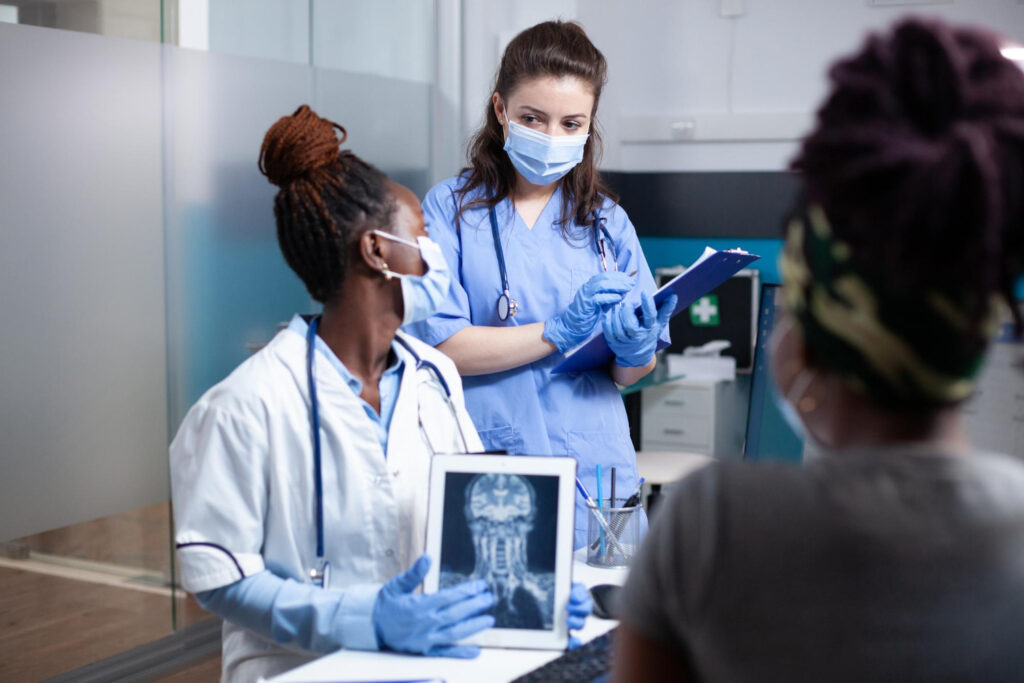 Three doctors in masks review medical imaging, discussing a patient's case.