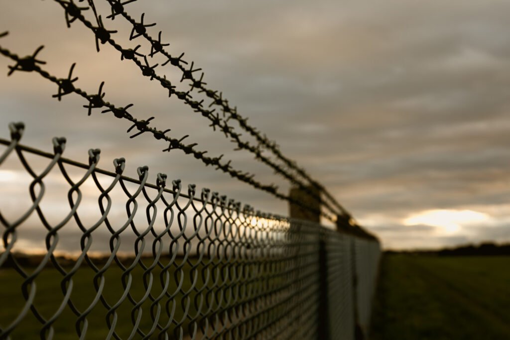 Chain link fence topped with barbed wire at sunset. Immigration detention.