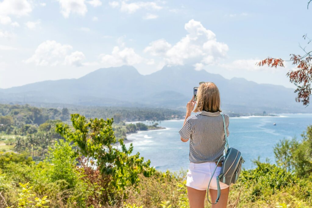 Woman taking a photo of a scenic ocean view from a hilltop.