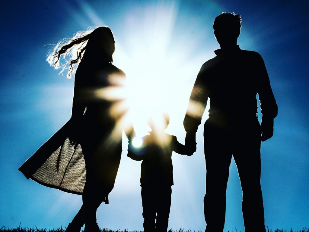 Silhouette of happy family holding hands, sun shining behind them. Australian family adopting a child.