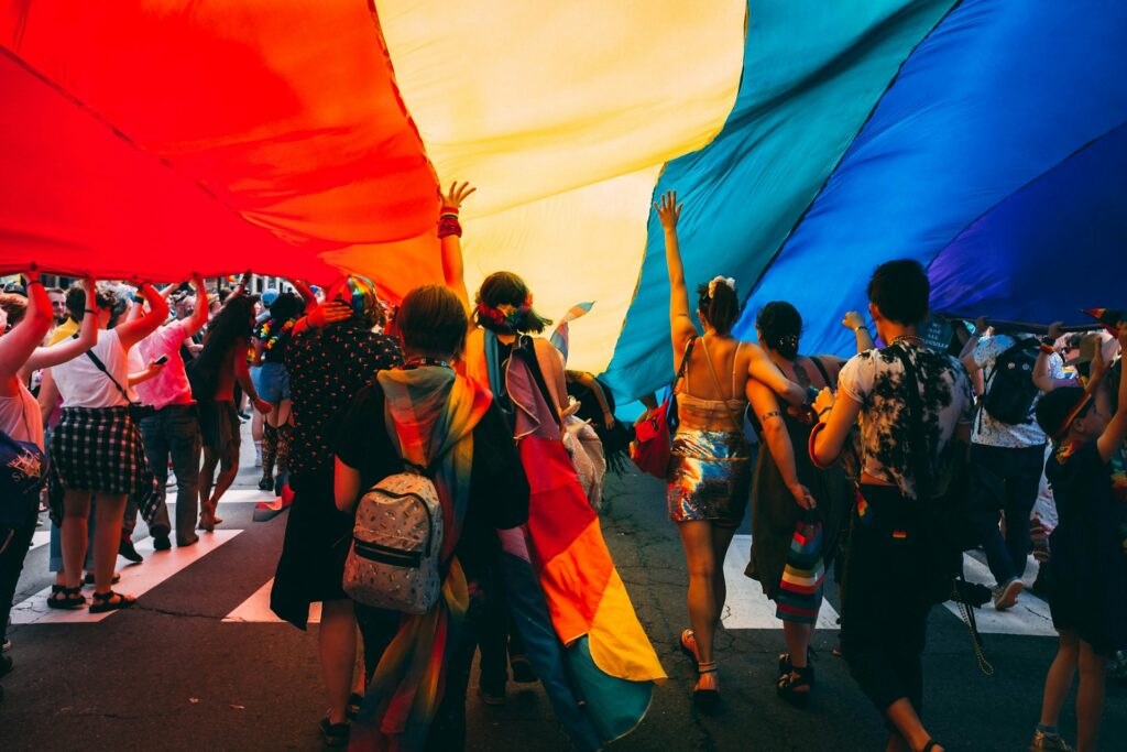 LGBTQ+ Pride parade participants carrying a large rainbow flag.