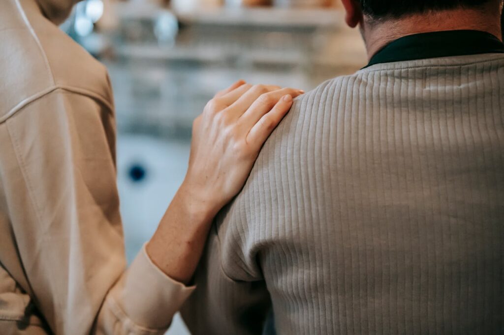A person comforting another with a hand on their shoulder.