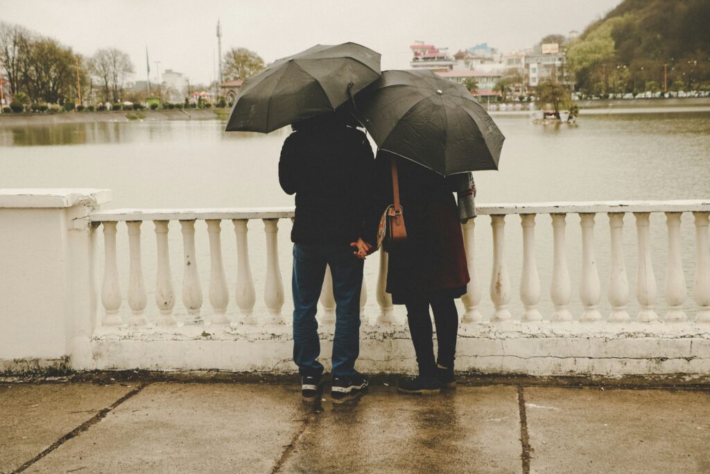 Couple holding hands under umbrellas by a lake.