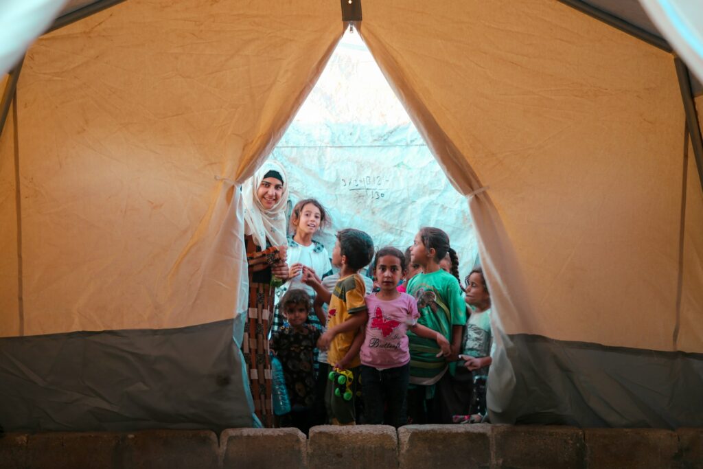 Refugee children in a tent with a woman, possibly a humanitarian aid worker.