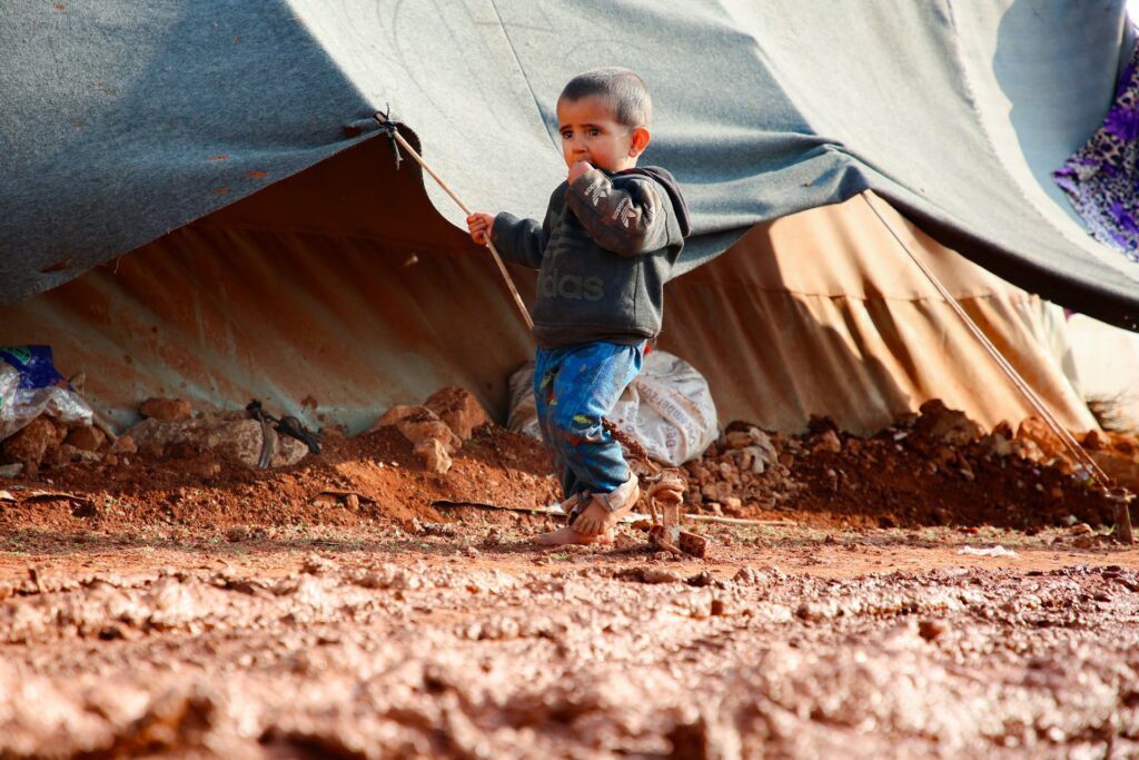 Young child playing near a temporary shelter, highlighting the plight of refugees seeking humanitarian visas like Subclass 449.