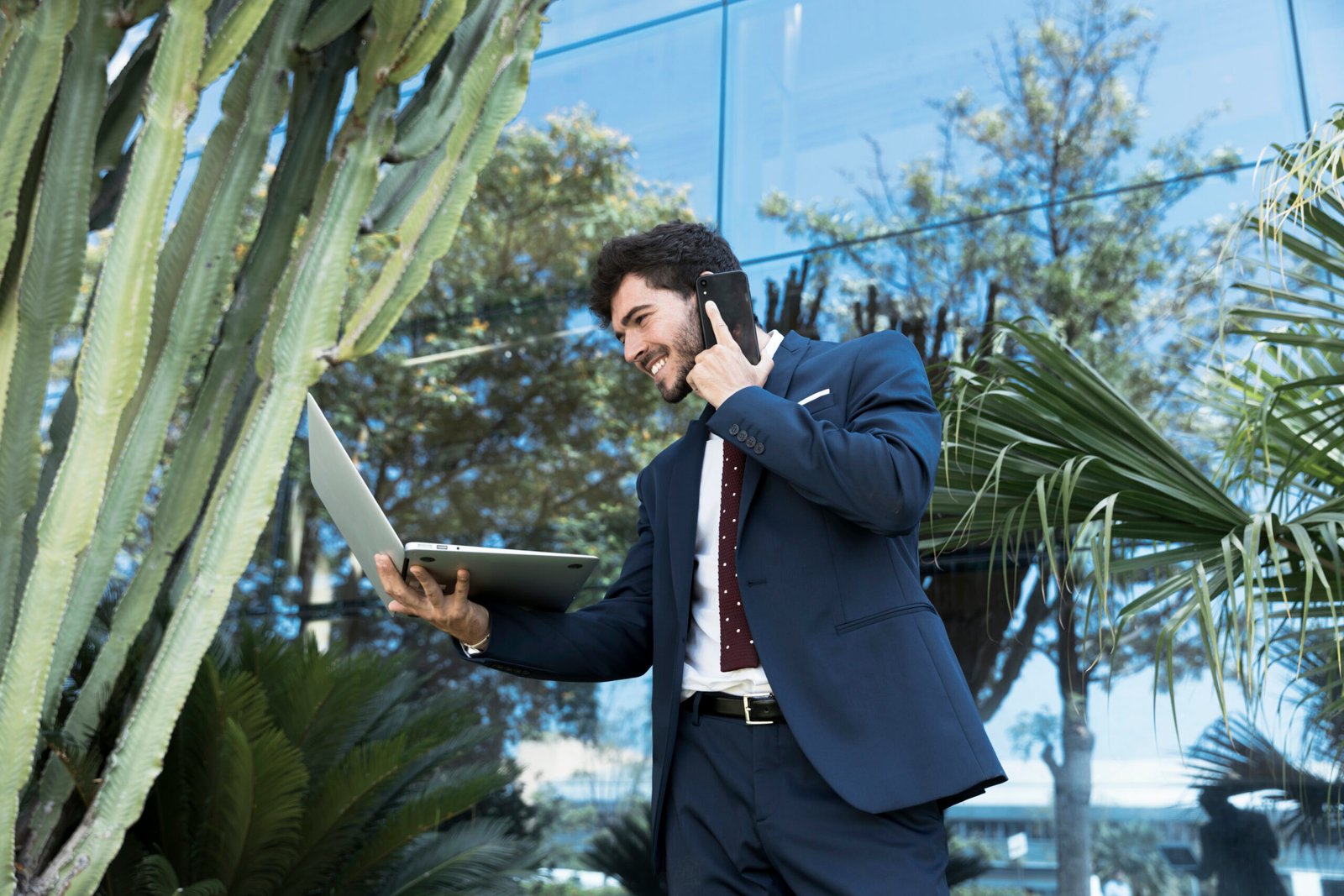 Businessman in suit using laptop and phone outside modern building