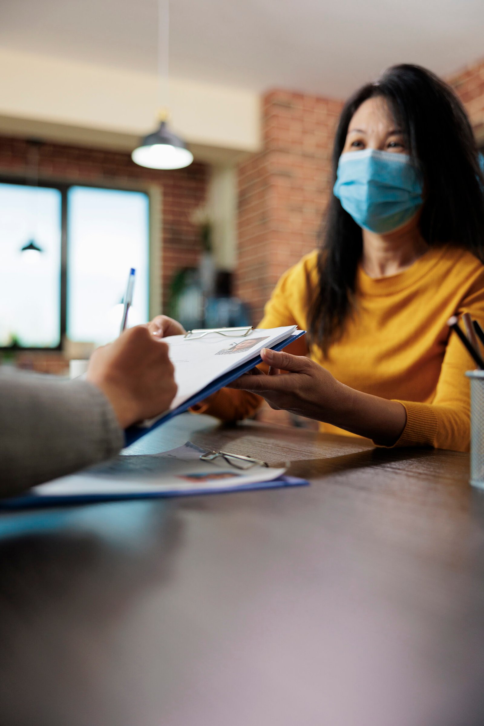 Woman in a mask receives paperwork from another person