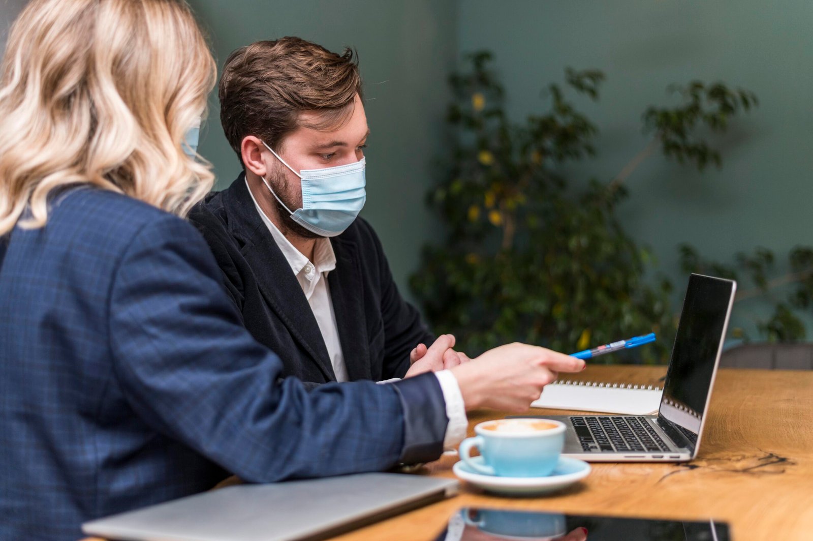 Two businesspeople in face masks collaborate on a laptop.