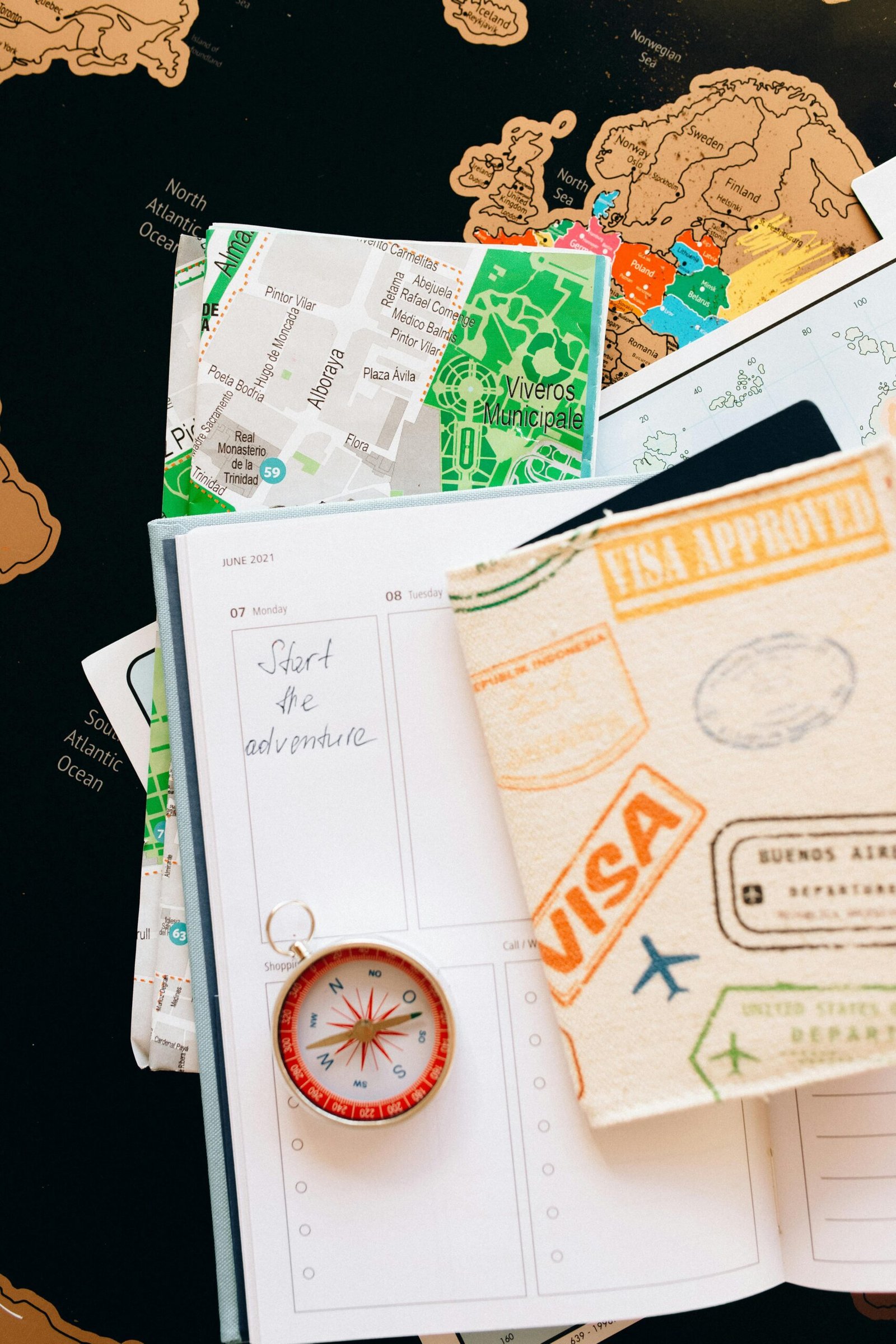 Passport with visa stamps, maps, compass, and planner; "Start the adventure" written in planner.