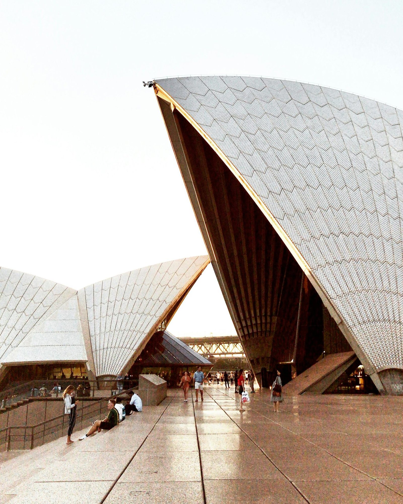 Sydney Opera House at sunset, people relaxing on plaza.