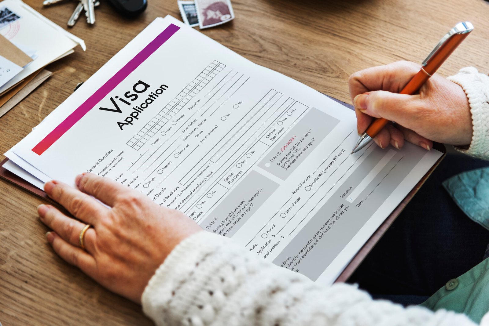 Person filling out a visa application form on a wooden desk