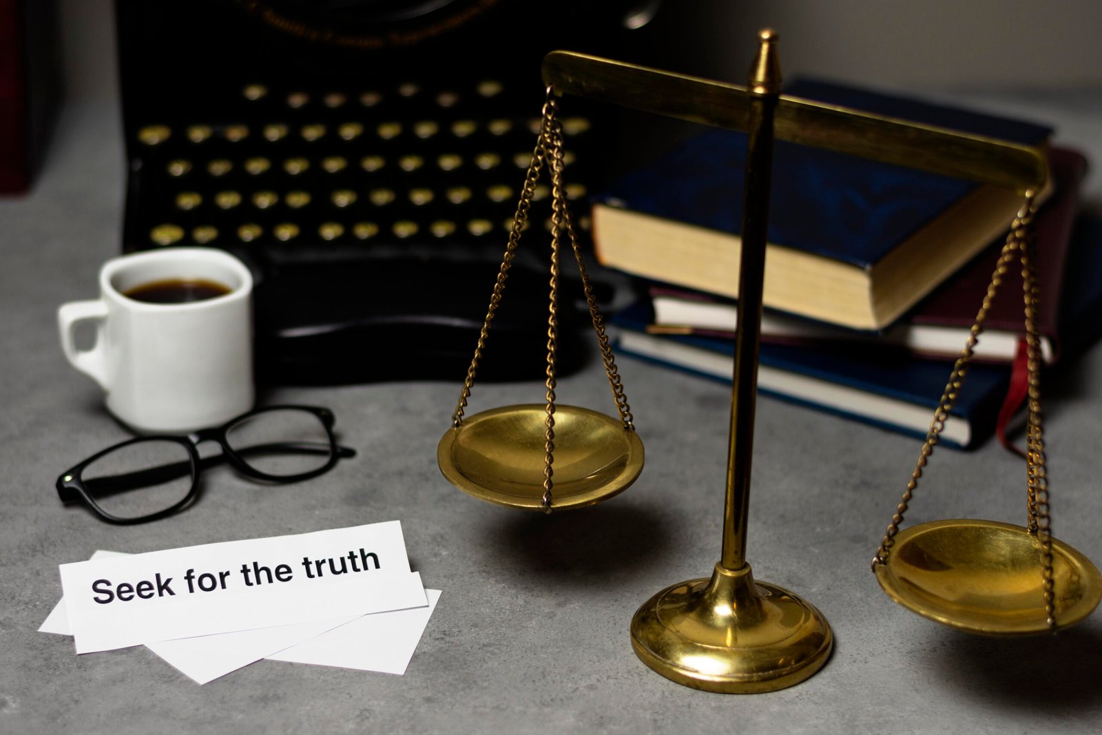 Scales of justice, glasses, coffee, and "Seek for the truth" text on a desk with a typewriter and books.