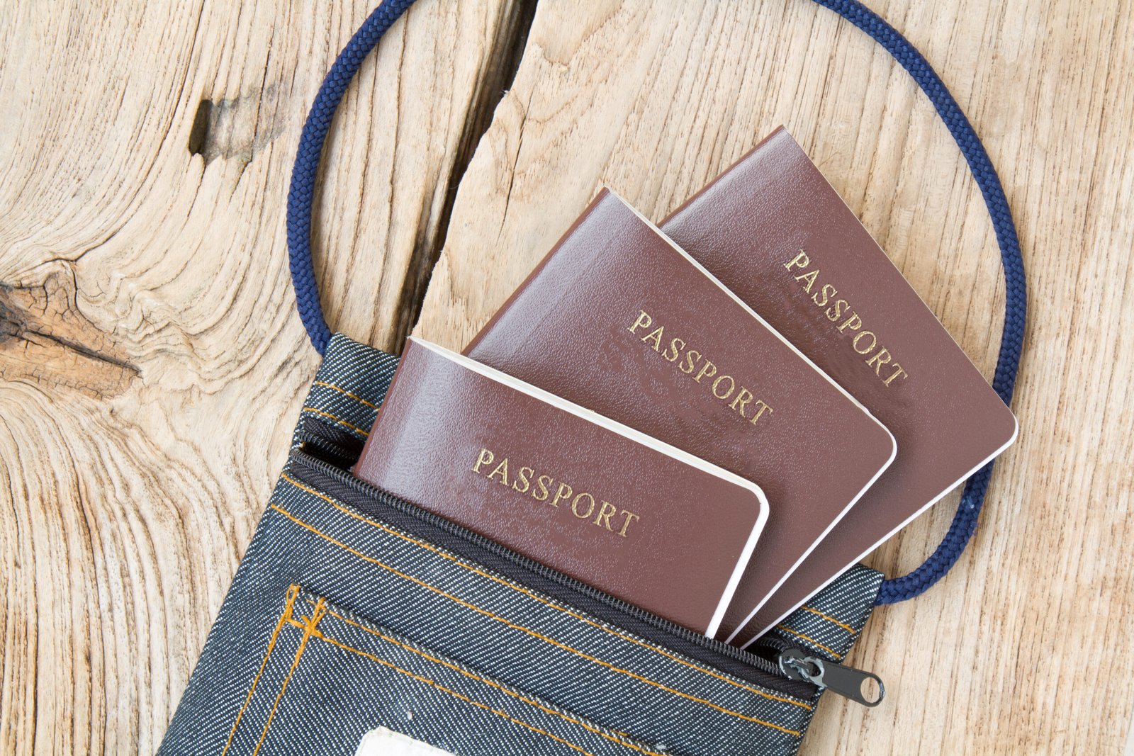 Passports in a small denim bag on a wooden surface.